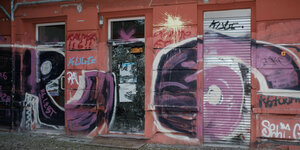 Eine Hausfassade ist mit Grafitti und Farbbomben bedeckt.