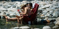 Ein Mann und zwei Frauen sitzen auf Plastikstühlen und kühlen sich im kalten Wasser des Lynn Creek ab