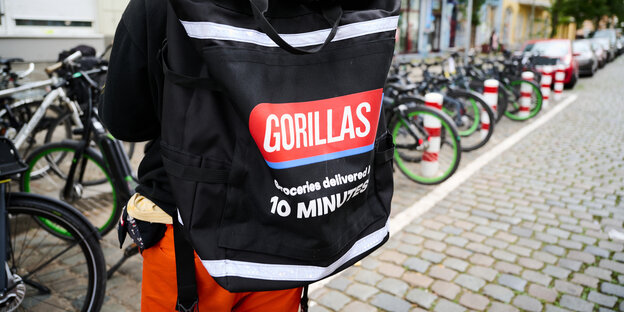 Eine Person mit Liefer-Rucksack von hinten, im Hintergrund Fahrräder