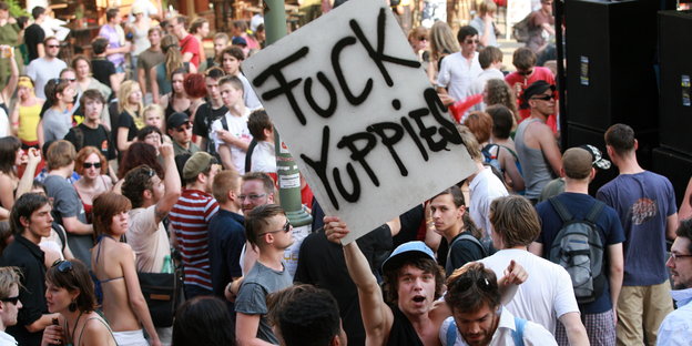 Demonstrant hält Plakat mit Inschrift "Fuck Yuppies" hoch