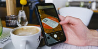 Ein Tisch in einem Café, eine Hand hält ein Handy in der Hand auf dem sich dank QR-Code die Luca-App öffnet