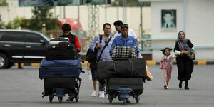Vier Männer, eine Frau mit Kopftuch und ein Mädchen mit zwei voll bepackten Gepäckwagen auf dem Flughafen von Kabul