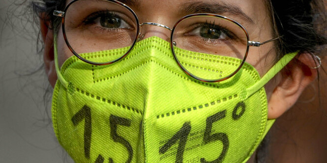 Junges Mädchen mit Brille und Maske, auf der steht: 1,5 Grad