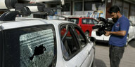 Ein Mann mit eienr KAmera in der Hand filmt vor einem Auto, dessen Scheibe durch Schüsse zerstört wurde.