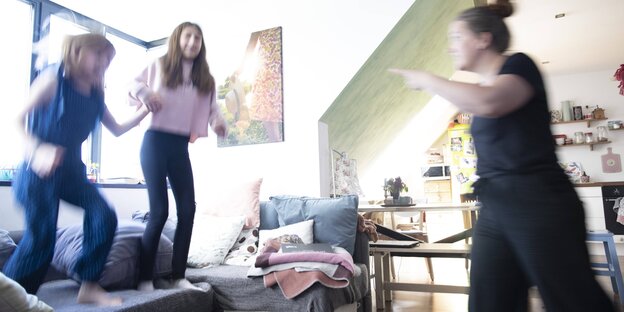 2 Mädchen hopsen auf dem Sofa, eine Mutter schimpft