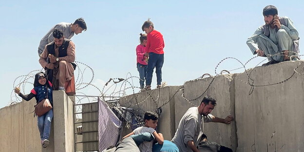 Männer versuchen Kinder über eine Mauer zu ziehen