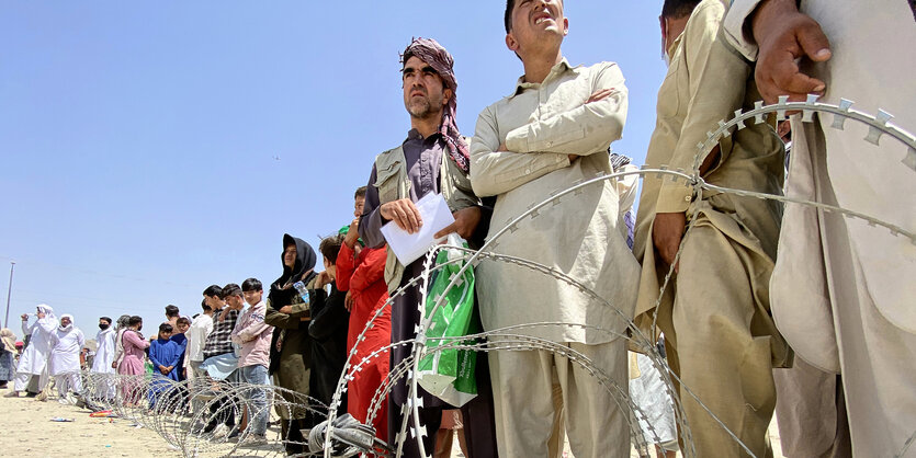 AfghanInnen stehen aufgereiht hinter einer Rolle Stacheldraht