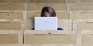 Studentin sitzt im Hörsaal und verdeckt ihr Gesicht mit Laptop