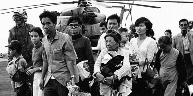 Eine zahlreiche Gruppe von Geflüchteten Vietnamesen stehen vor einem gelandeten Hubschrauber