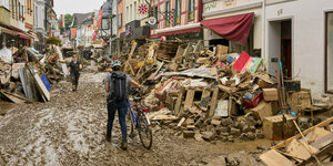 Altstadtgasse von Ahrweiler mit Müll und Matsch, eine Frau schiebt ihr Frahrrad