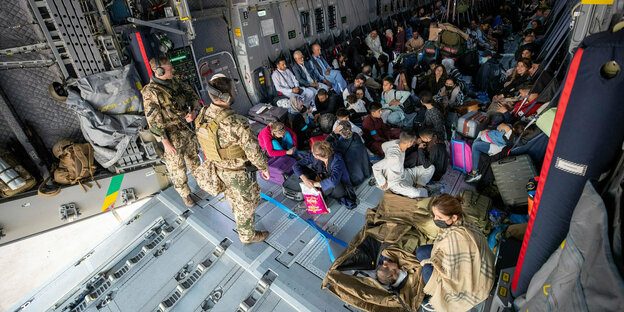 Menschen sitzen dicht gedrängt auf dem Boden einer Militärmaschine