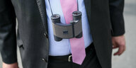 Ein Mannerkörpger im Anzug: Vor der Krawatte baumelt ein Fernglas