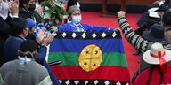 Eine Frau, Elisa Loncon, hält in einem Versammlungssal eine blau-grün-rote Fahne