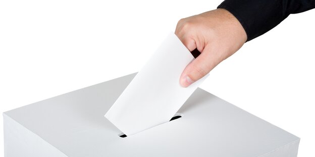 Eine Hand wirft einen Umschlag in den SChlitz einer Wahlurne