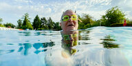 Der Kopf eines alten Mannes mit Schwimmbrille lugt aus blauem Wasser