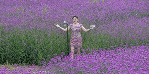 Eine Frau steht mit ihrer Kamera in einem lila Blumenfeld und filmt sich