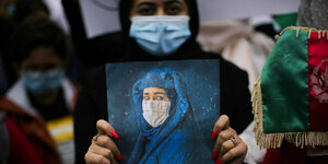 Eine afghanische Frau hält das Bild einer weinenden Frau in Burka vor sich
