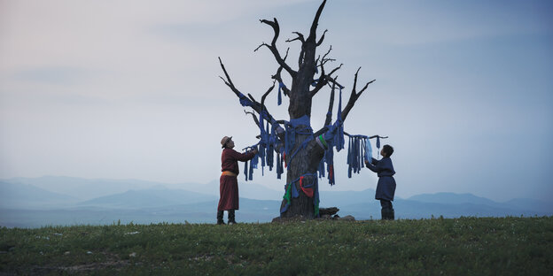 Ein Mann und ein Kind knoten Stoffe an einen kahlen Baum, der als Gebetsbaum dient