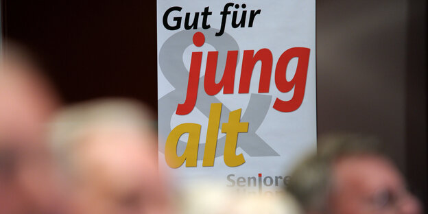 Köpfe mit weißen Haaren vor einem Plakat mit der Aufschrift "Gut für jung & alt"