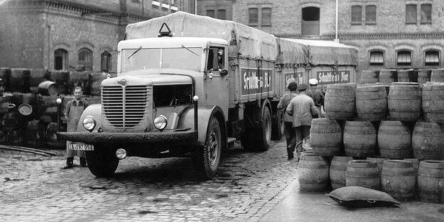 Das alte schwarz-weiße Foto zeigt einen altmodischen Lastwagen der Berliner Schultheiss-Brauerei zwischen Bierfässern in den späten 1940er Jahren.