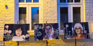 Porträtfotos von zwei Frauen und einem Mädchen hängen vor einer Hauswand