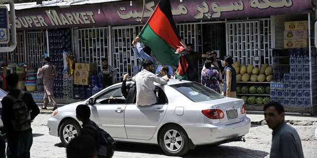 Männer sitzen im Fenstter eines Autos mit der Nationalfahne Afghanistans