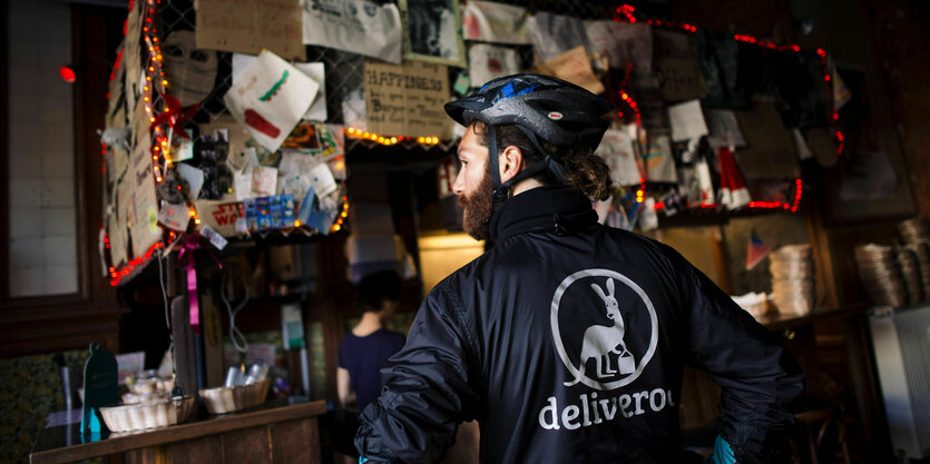 Ein Mann mit einer Deliveroo-Jacke steht vor einem Kneipentresen