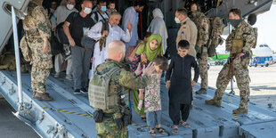 Menschen steigen aus einer Bundeswehrmaschine, Kinder schauen auf einen deutschen Sodaten, der etwas erklärt