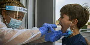 Eine Frau mit schutzschirm testet einen kleinen Jungen, der den Mund aufreißt
