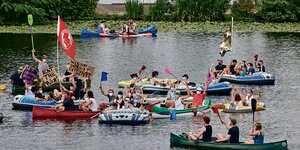 Demonstanten sitzen in bunten Kanus und Schlaubooten auf dem Wasser