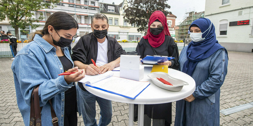 Mehre Menschen stehen um einen Stehtisch herum und fülllen einen Fragebogen aus.