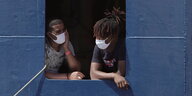 Zwei Menschen mit Mundschutz schauen durch eine blaue Schiffsluke