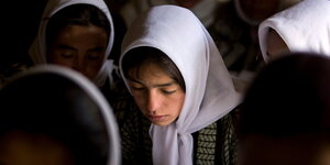 Ein Mädchengesicht unter einer weißen Kopftuchhaube, im Hintergrund weitere Mädchen
