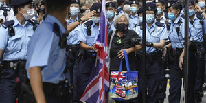 Eine ältere Frau mit Union Jack Flagge und Tasche wird von Polizisten eingekreist