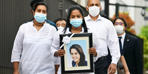 Das Foto einer jungen Frau, umgeben mit einem Trauerflor inmitten einer Gruppe vor Protestierenden