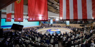 Ein großer, gut besetzter Konferenzsaal mit vielen Nationalflaggen.