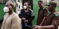 Freeman Mbowe wird aus einem Auto eskortiert. Hinter ihm gehen zwue Soldataen in Uniform Mbowe und ein weiterer Mann tragen Masken.