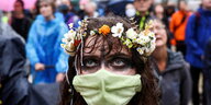 Protestierender mit Blumenkranz und grüner Maske