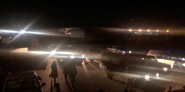 Unter Scheinwerfern laufen Menschen in Richtung eines Flugzeugs