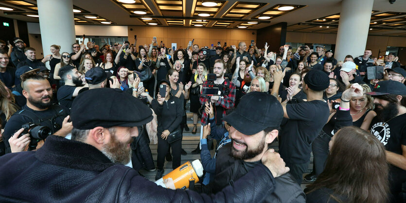 Zahlreiche Menschen stehen lächelnd und triumphierend in einem Foyer