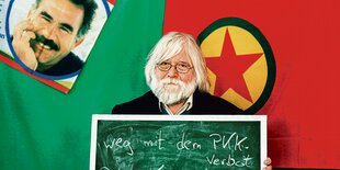 Robert Jarowoy steht vor einem Bild von Abdullah Öcalan und einer Flagge der Kurdisch Demokratischen Gesellschaft und hält eine Tafel mit der Aufschrift: "Weg mit dem PKK-Verbot".