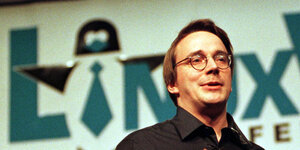 Linus Torvalds, Erfinder von Linux, spricht vor einem Banner, das "Linux" zeigt. Das I ist als Tux verkleidet, das Pinguin-Maskottchen von Linux