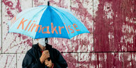 ein Demonstrant hält bei einer Protestaktion vor der CDU-Parteizentrale einen hellblauen Regenschirm hoch, der die Aufschrift "Klimakrise" trägt