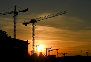 Das Foto zeigt Baukräne vor untergehender Sonne.