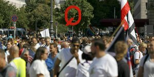 Mehrere Menschen auf einer Demonstration. Im Hintergrund eine Reichsflagge und ein großes "Q"-Schild, das für die rechte verschwörungsideologische QAnon-Bewegung steht.