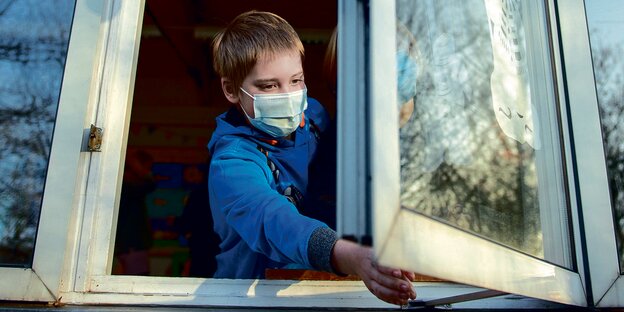Ein Schüler mit Maske öffnet das Fenster eines Klassenzimmers.