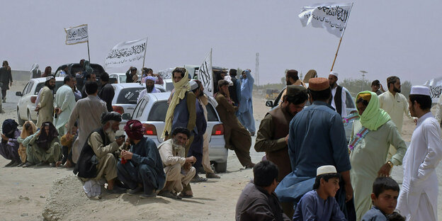 Männer halten die Fahnen der Taliban in die Höhe, andere kauern sitzend herum