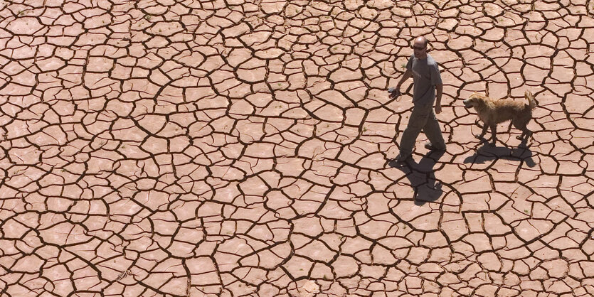 Das Foto zeigt einen Mann mit Hund in ausgedörrter Landschaft.