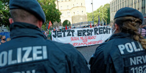 Zwei PolizistInnen stehen vor Menschen mit einem Transparent gegen gegen Polizeigewalt