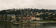 Eine Fernansicht der Ortschaft Loschwitz, unten im Bild ist ein Fluss mit Schiffen zu sehen, der unter der Stadt liegt